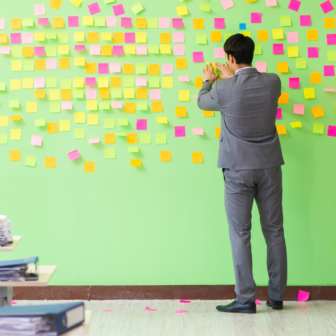 Man sorting through numerous post-it notes to prioritize tasks, symbolizing effective time and resource management for productivity enhancement.